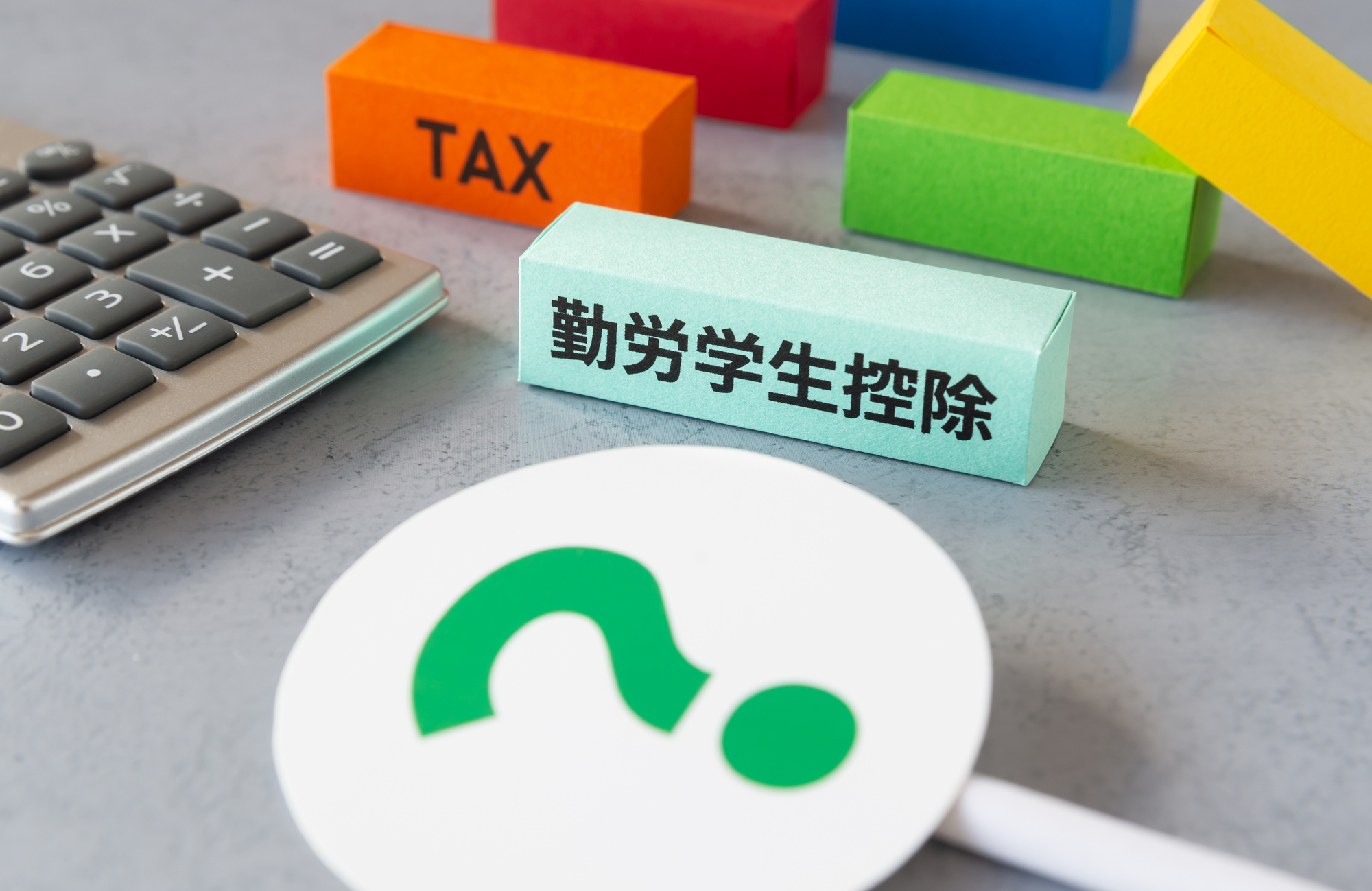 「？」と書かれた札と「TAX」「勤労学生控除」と書かれたブロック、電卓