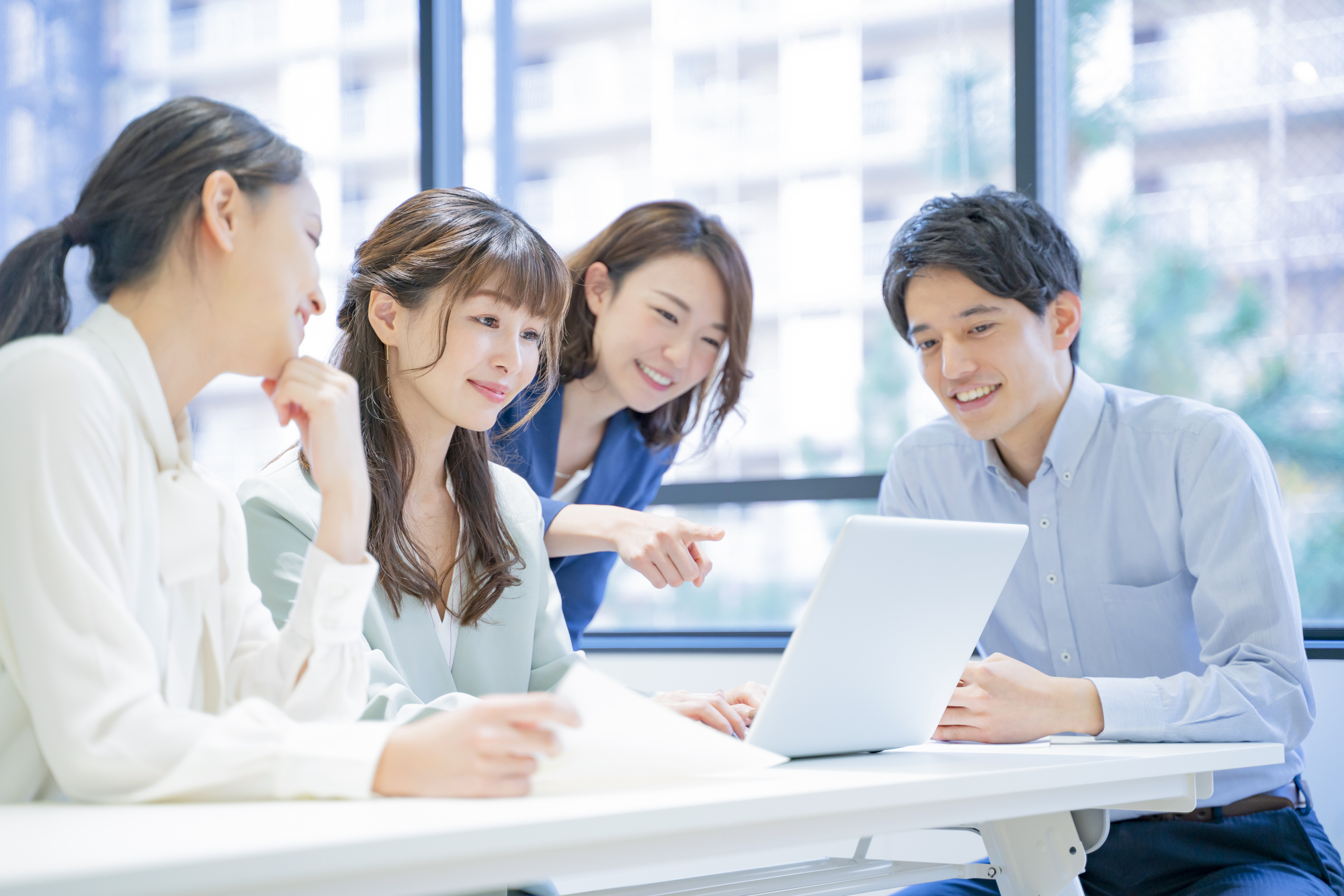 パソコンを囲みながら話し合う4人のビジネスパーソン