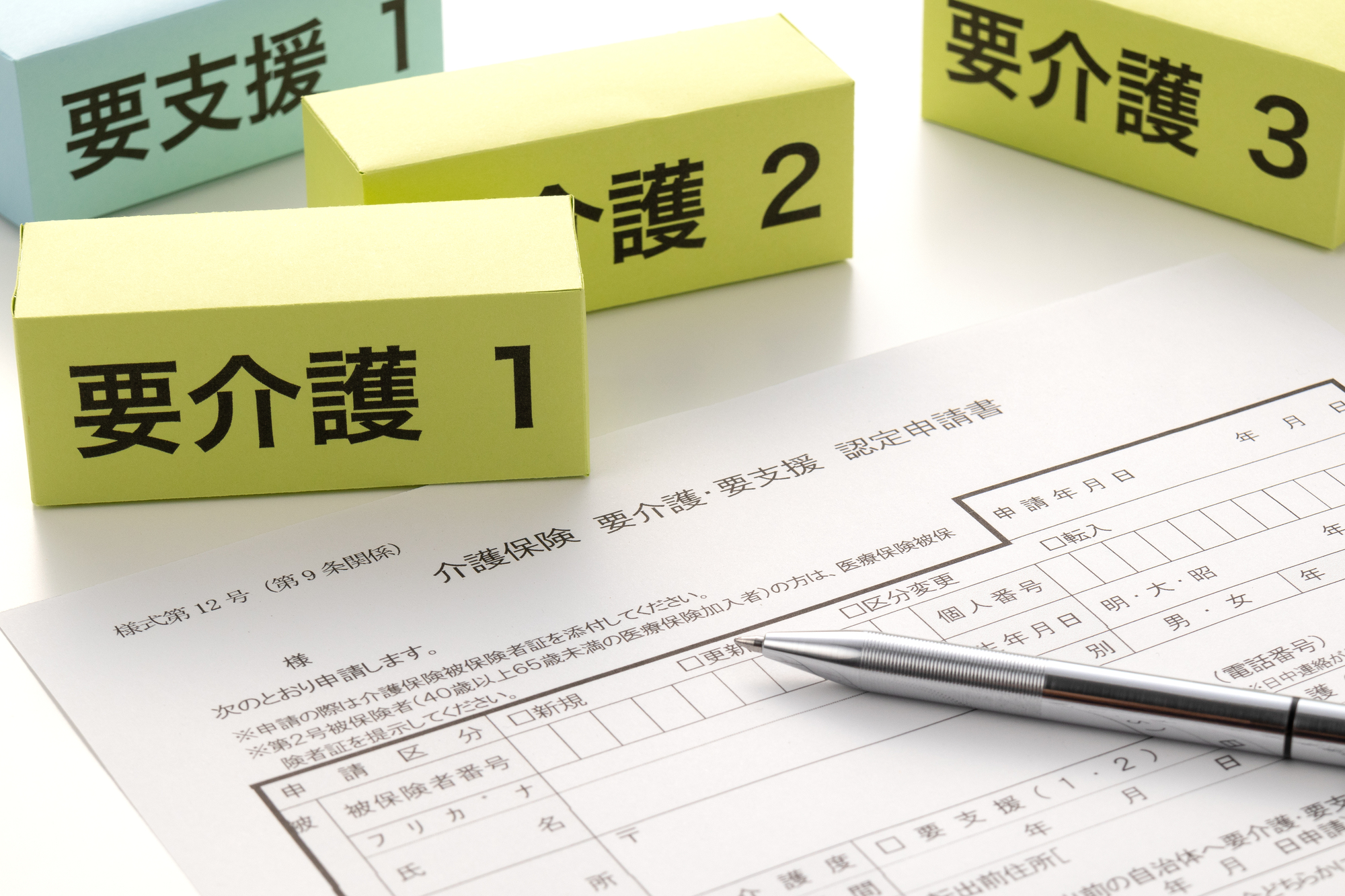 介護保険の認定申請書と「要介護」などと書かれたブロック、ボールペン