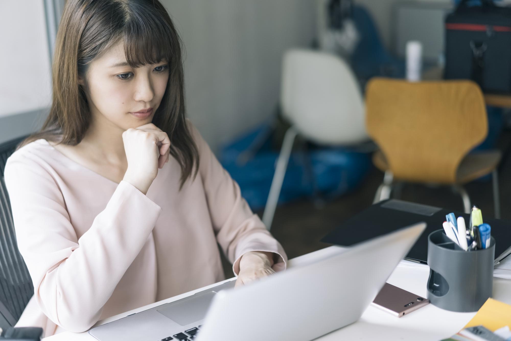 右手を顎に当て、パソコンを操作する女性