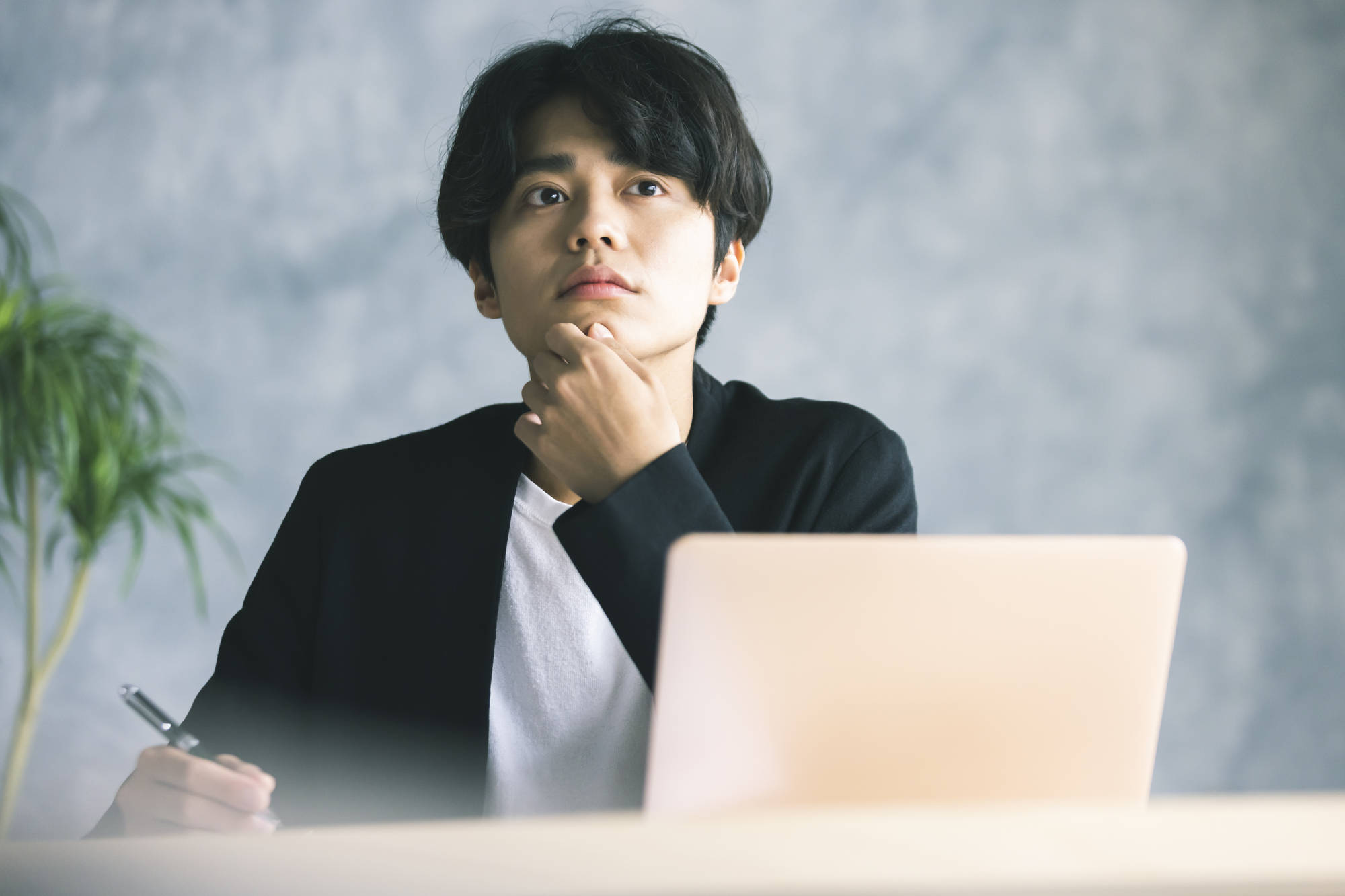 パソコンの前で考え事をしている様子の男性