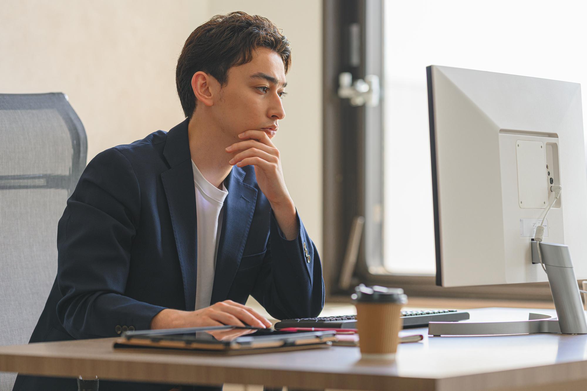 左手を顎に当て、真剣な表情でパソコンを見る男性