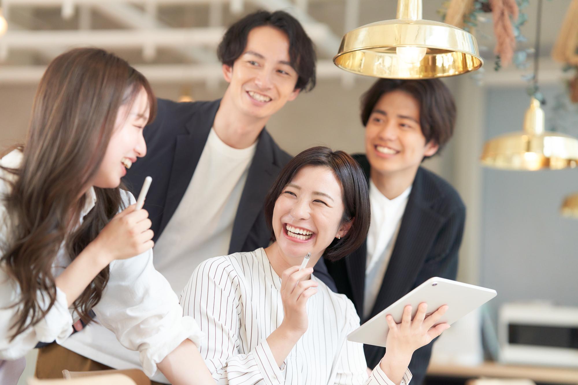 左手にタブレットを持つ女性と、その周囲に集まる笑顔の男女