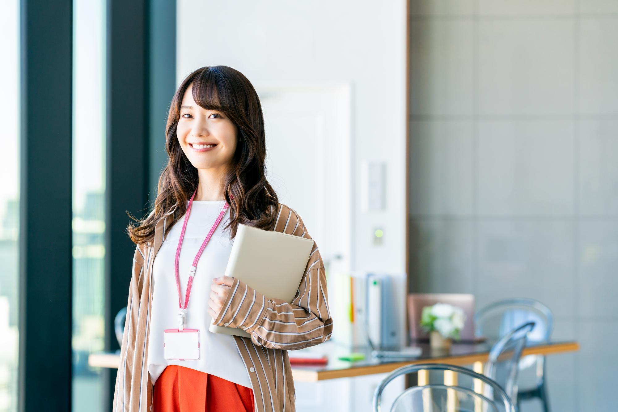 左手にファイルを持ち、社員証を首にぶら下げて笑顔でこちらを見る女性
