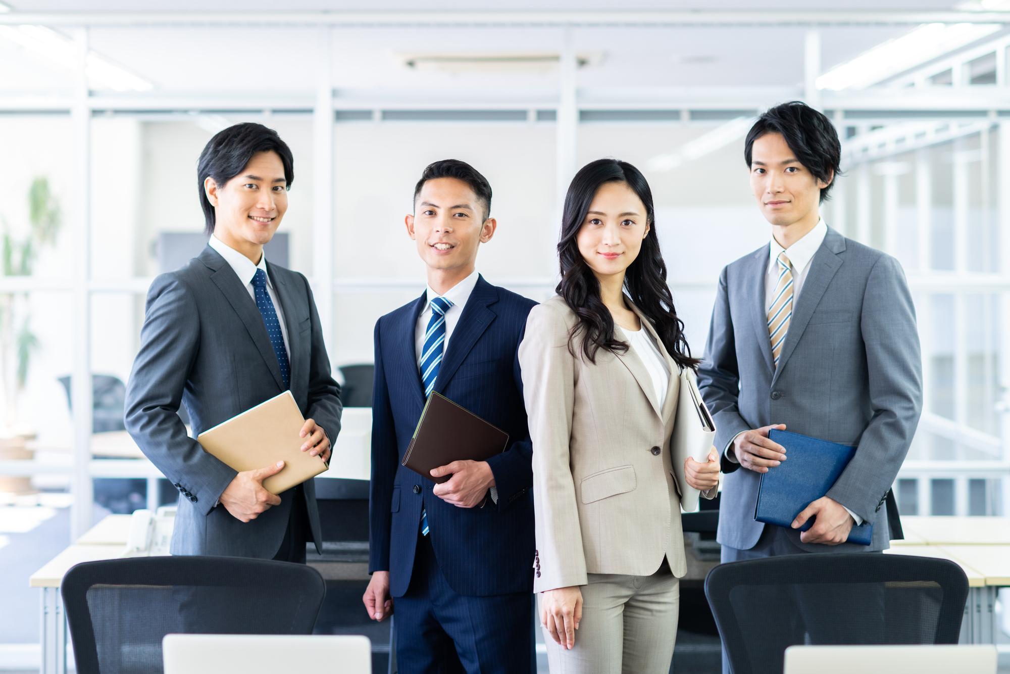 ファイルを持ってこちらを見つめるスーツを着た男女4人