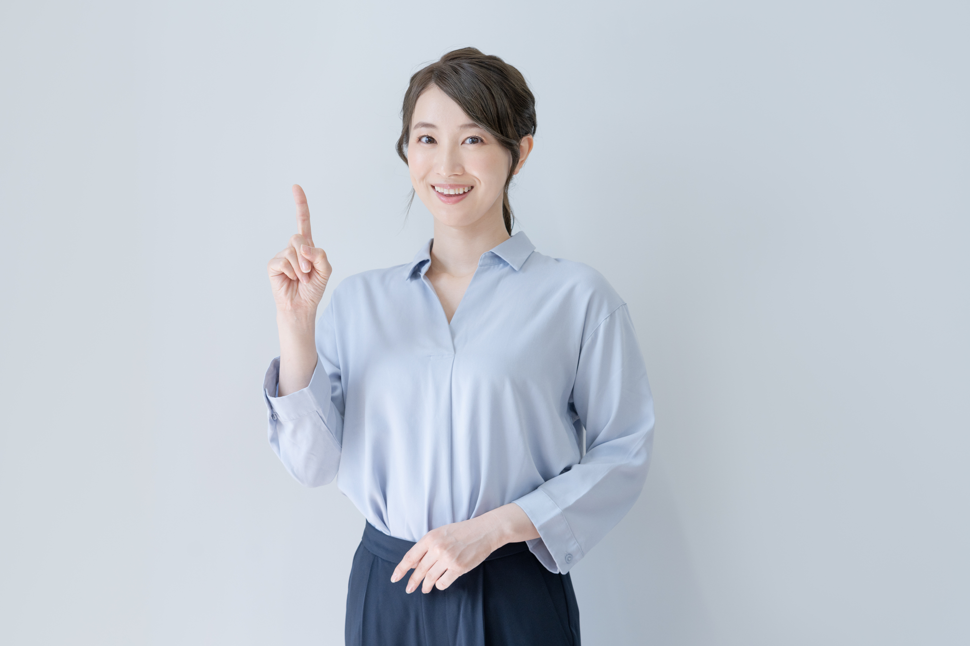 人さし指を立て、カメラ目線で笑顔を見せる女性ビジネスパーソン