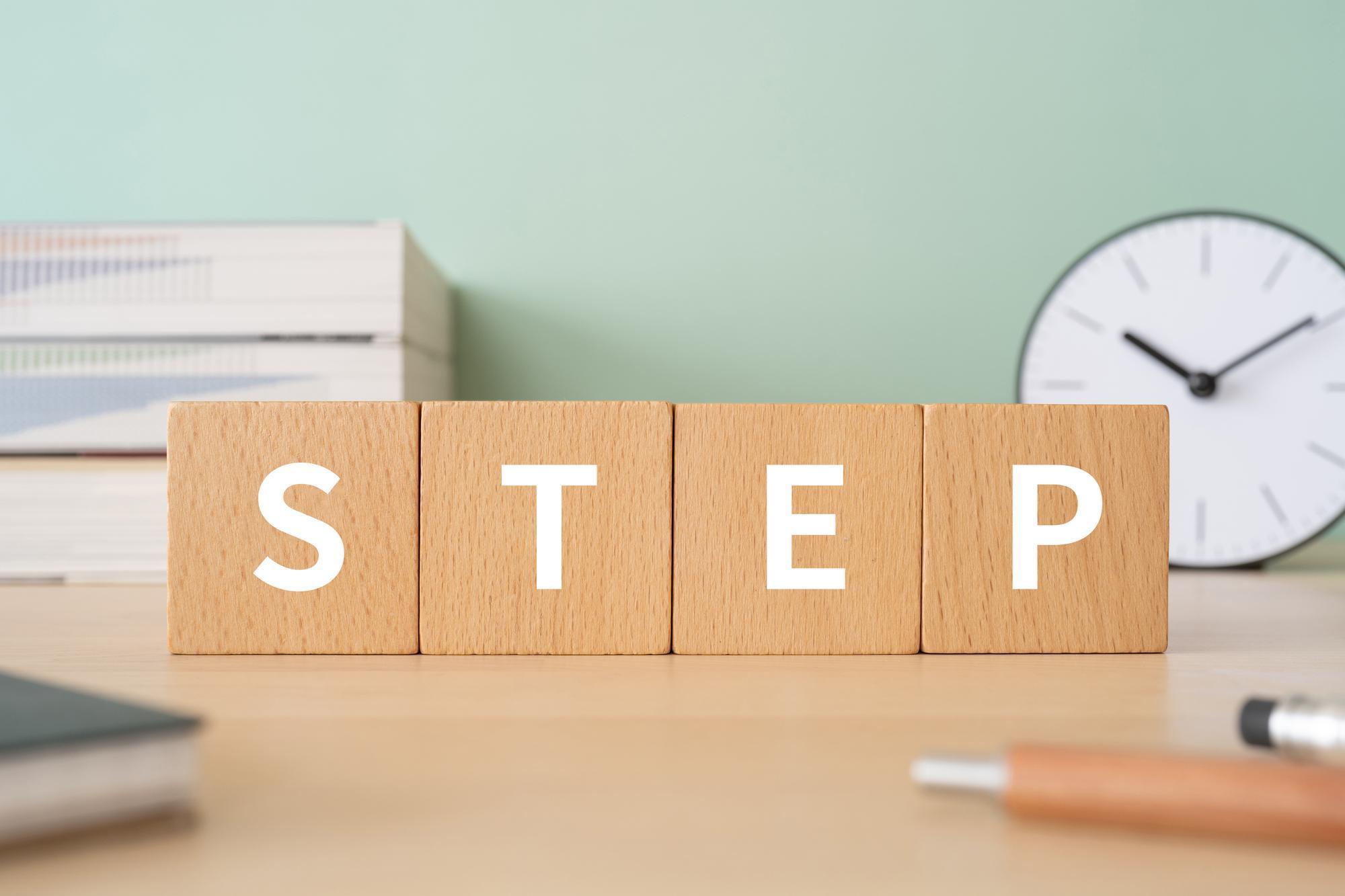 STEPと書かれた木のブロックと本やペンなどの小物