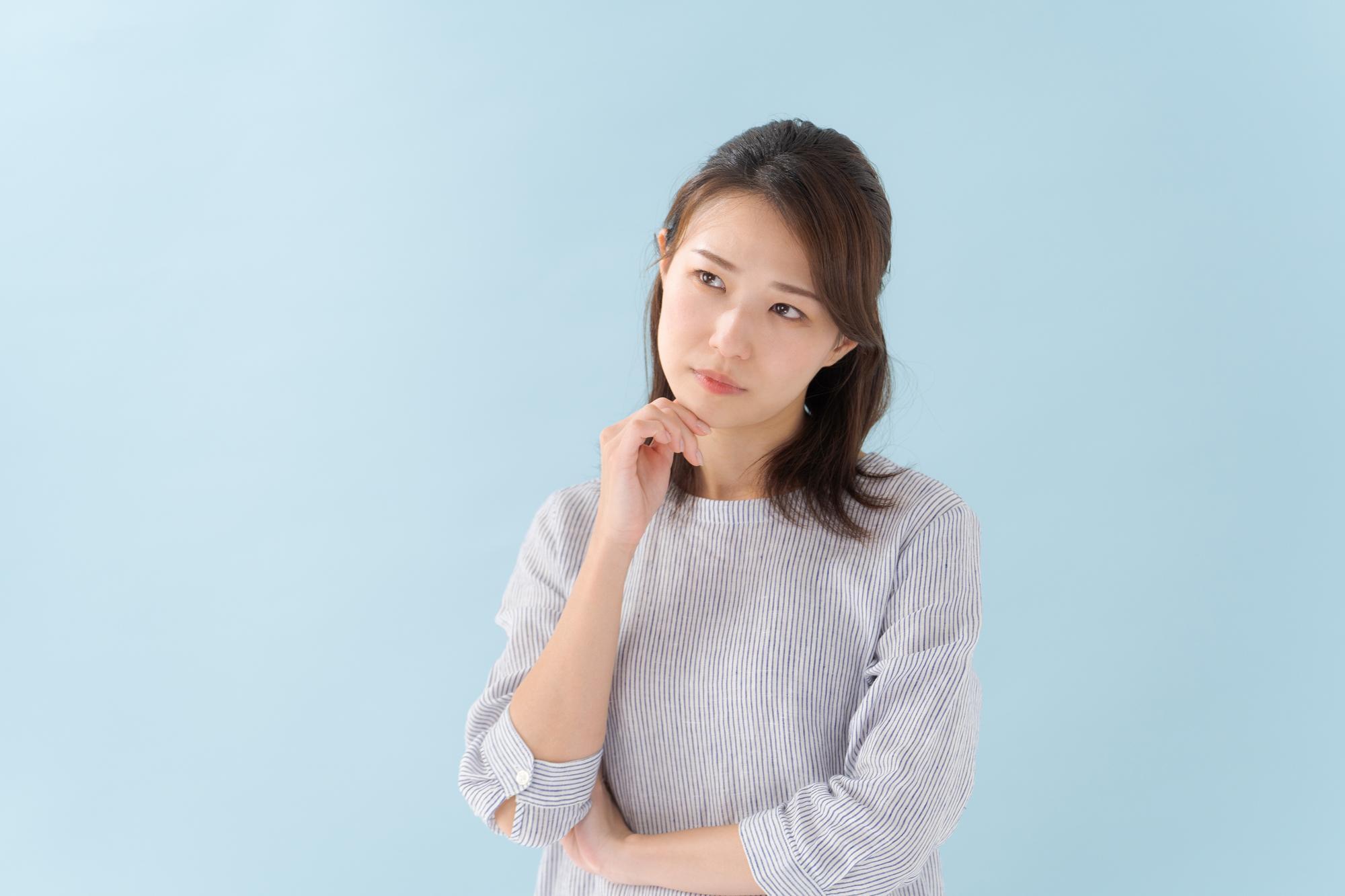右手を顎に当て首をかしげる女性