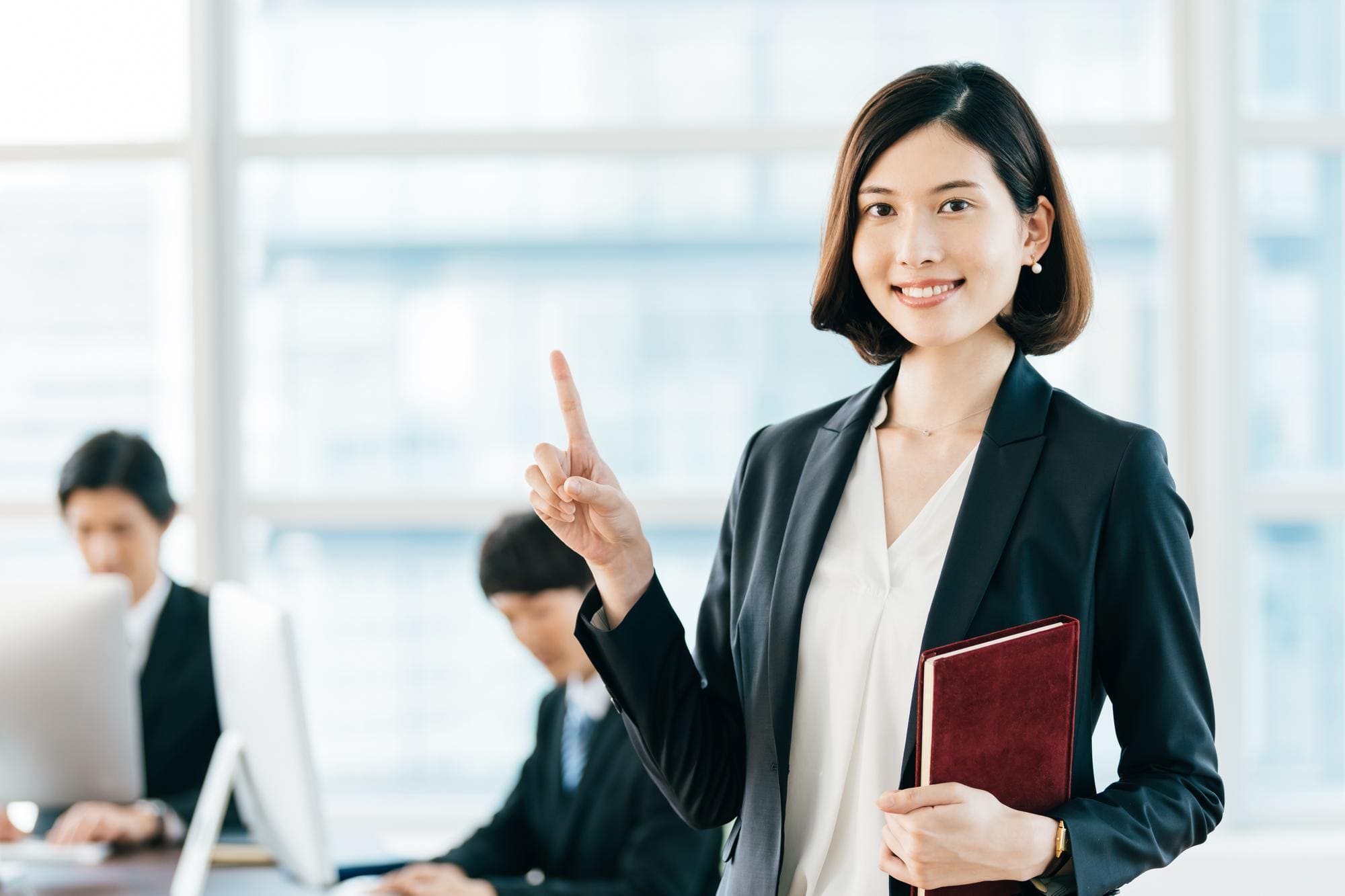 オフィスにて、人さし指を立て、笑顔を向ける女性