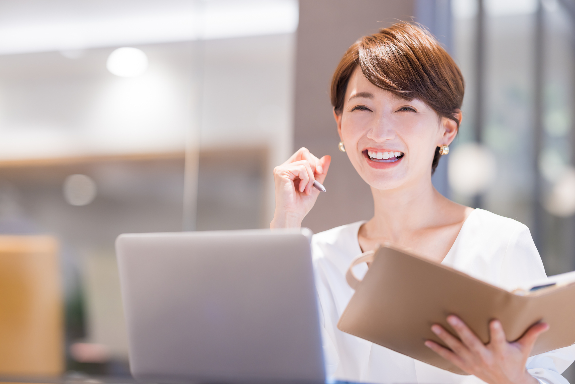 手帳とパソコンを前に笑顔を見せる女性ビジネスパーソン