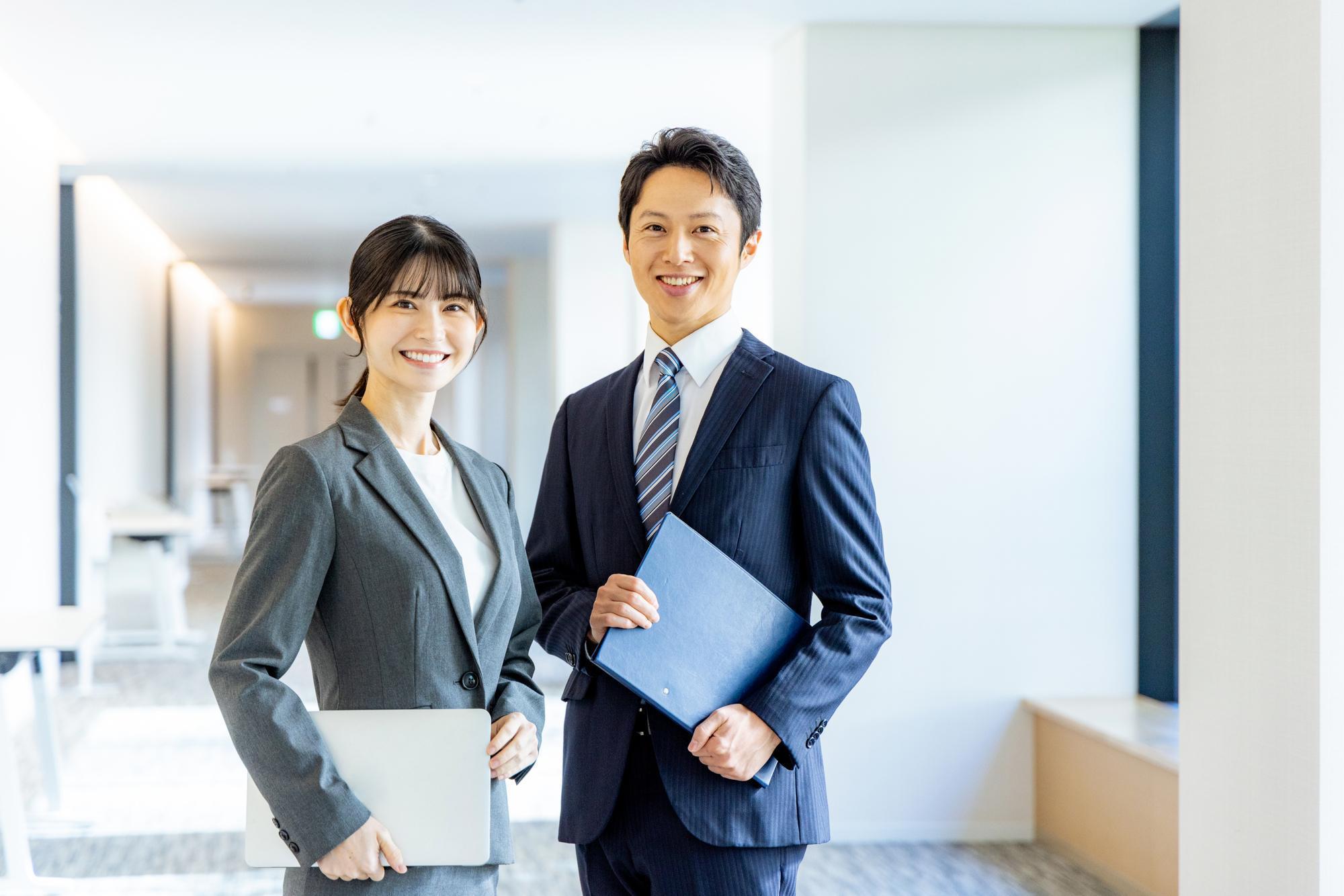 ファイルを持ち、笑顔を向けるスーツの男女