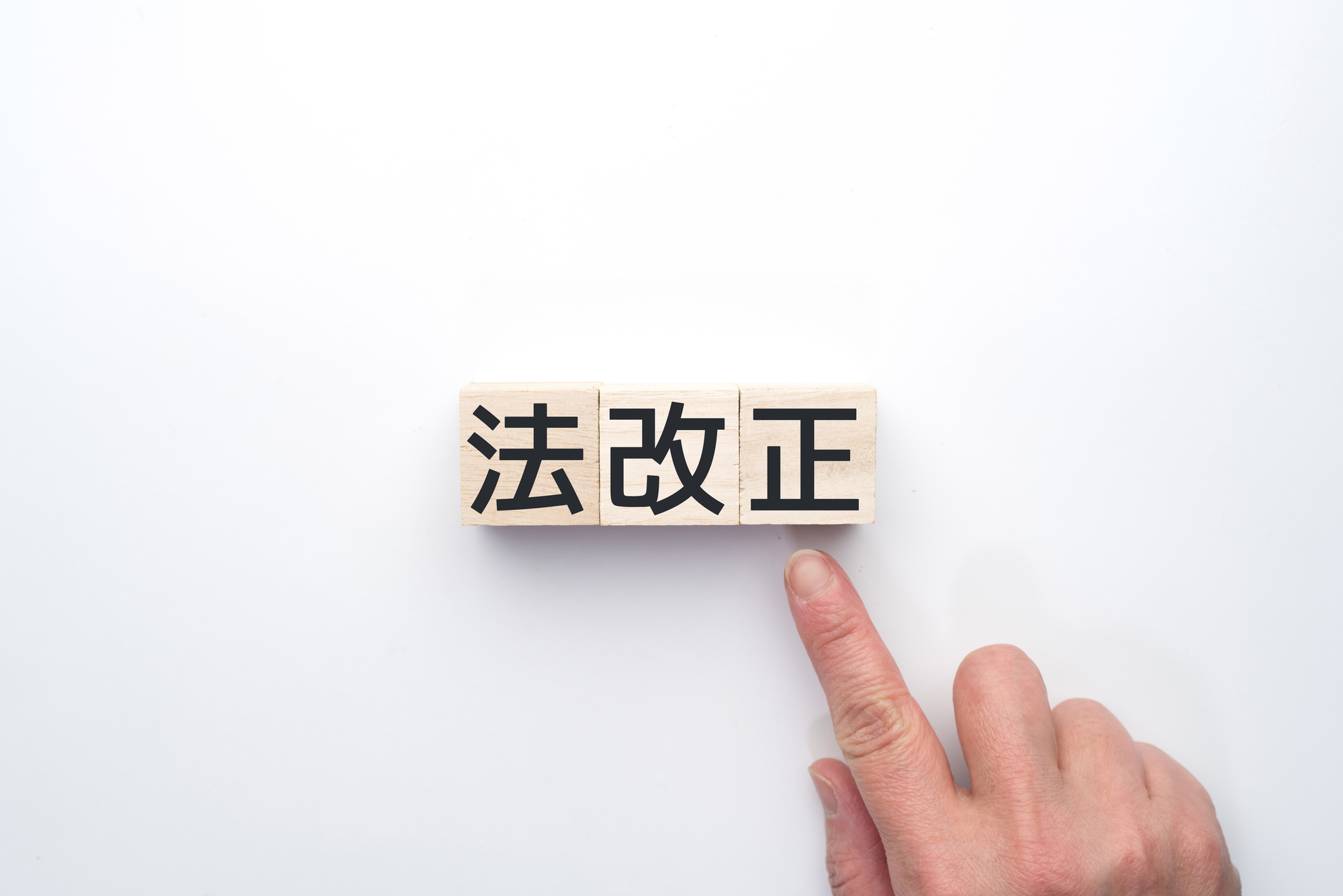 「法改正」と書かれたウッドブロックを指さす手