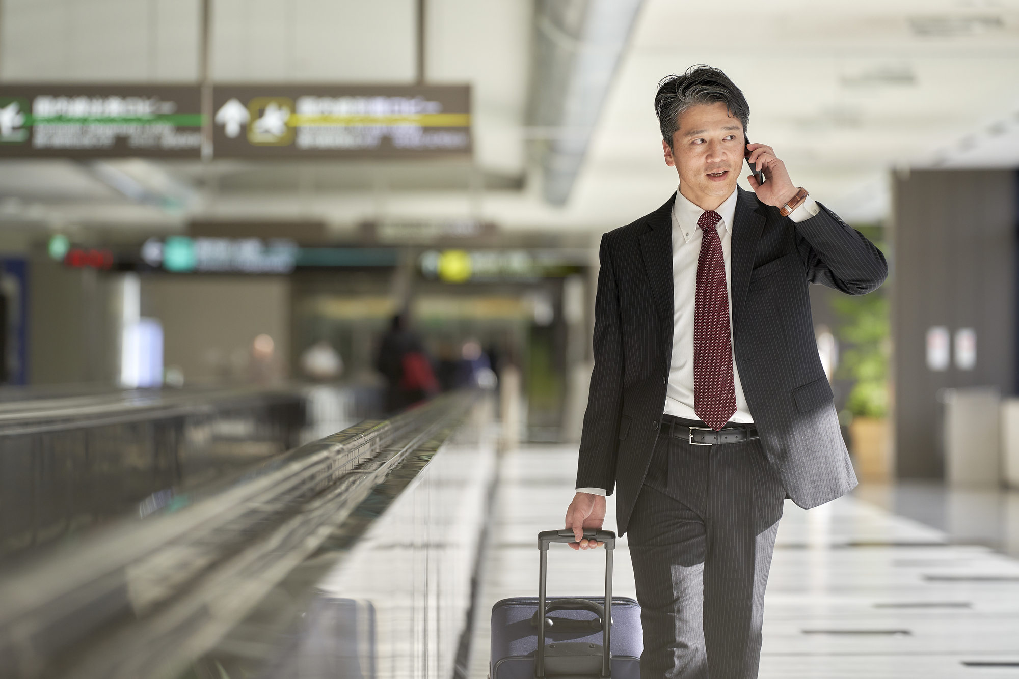 空港でスーツケースを引きながら電話する男性ビジネスパーソン