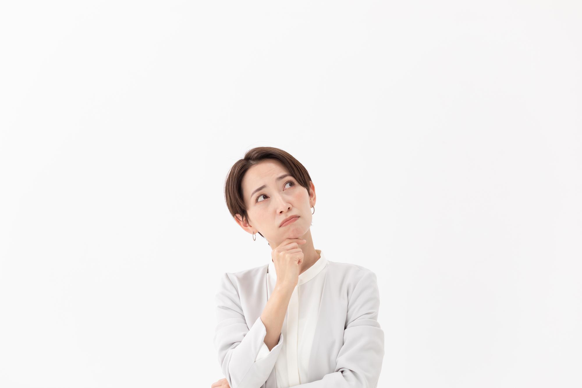 白の背景、右手を顎に当て、斜め上を見る女性