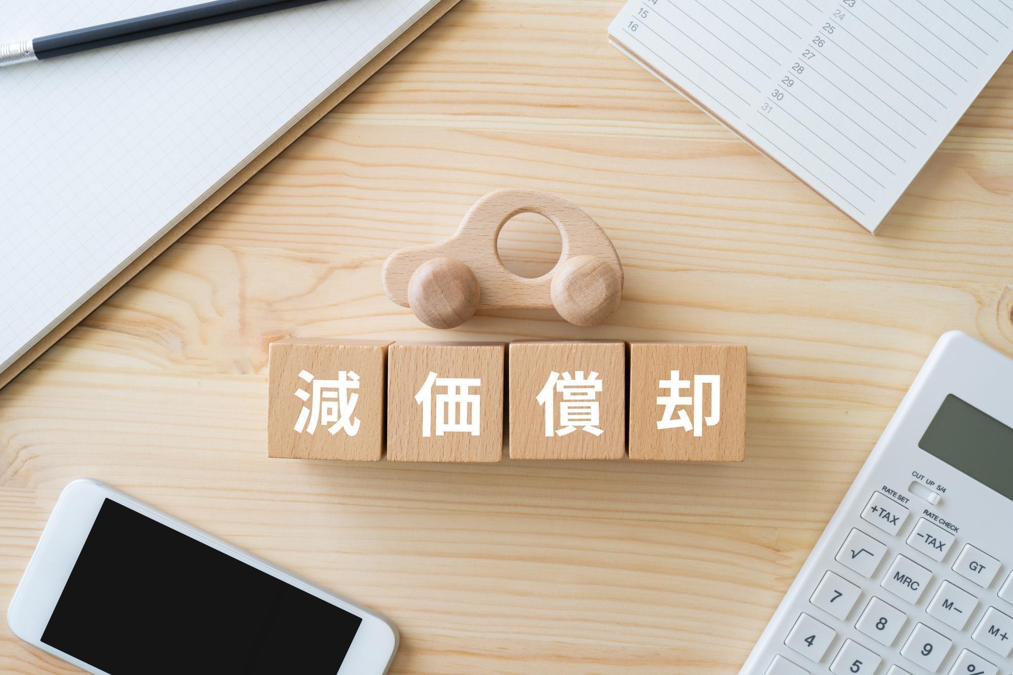減価償却と書かれた木のブロック、ノート、スマホ、電卓