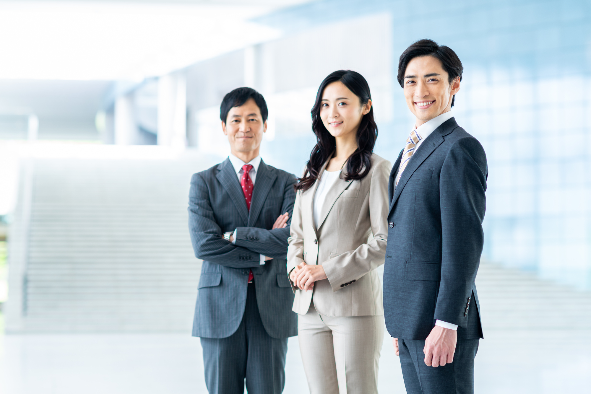 オフィスに笑顔で並ぶ3人のビジネスパーソン